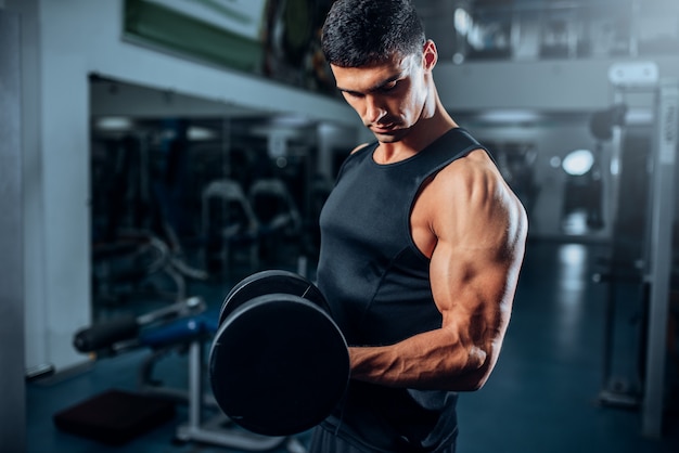 tanned-muscular-athlete-workout-with-dumbbell-gym_266732-275